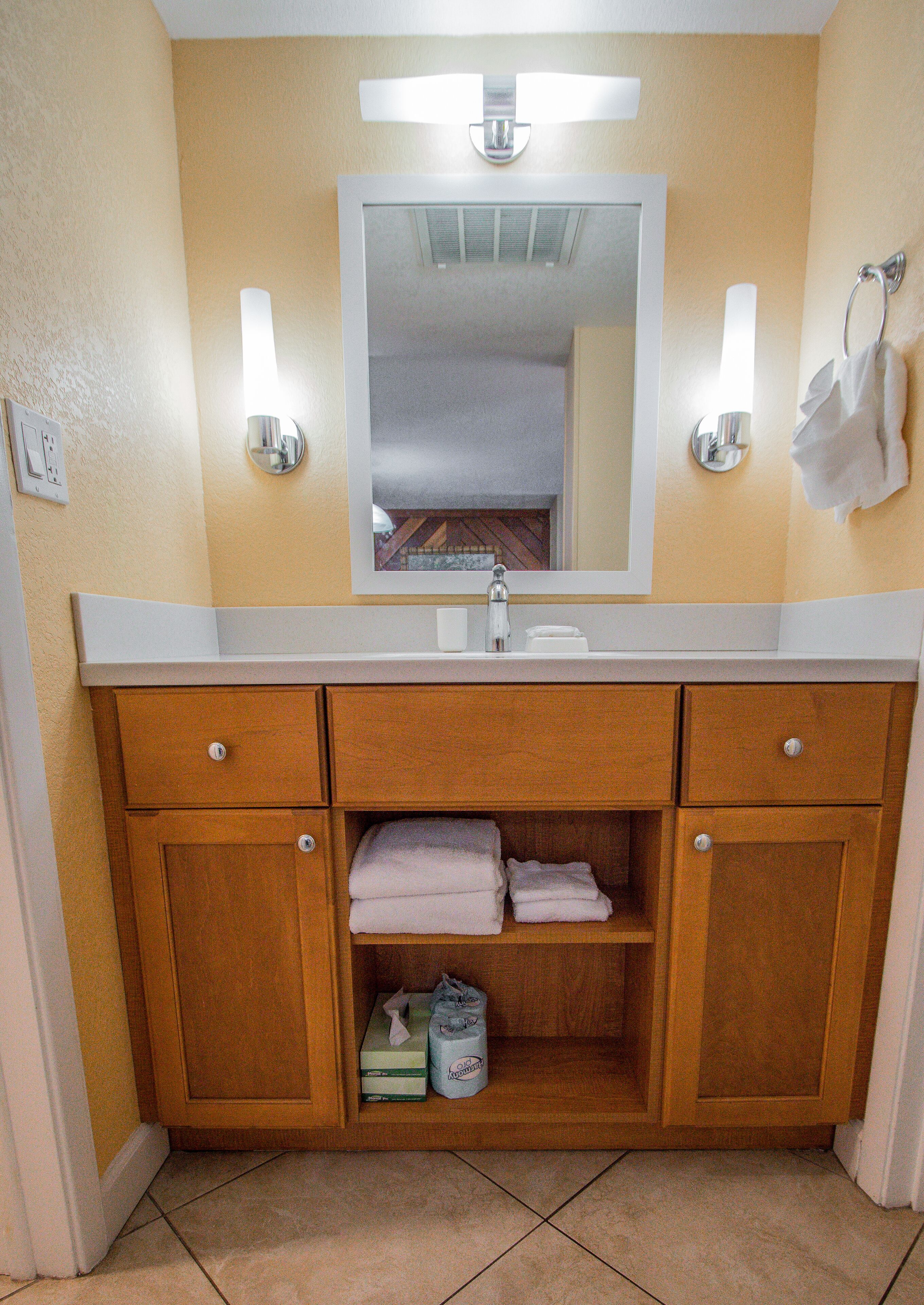 A bathroom with a wooden vanity, a mirror, two wall-mounted lights, and a towel rack.