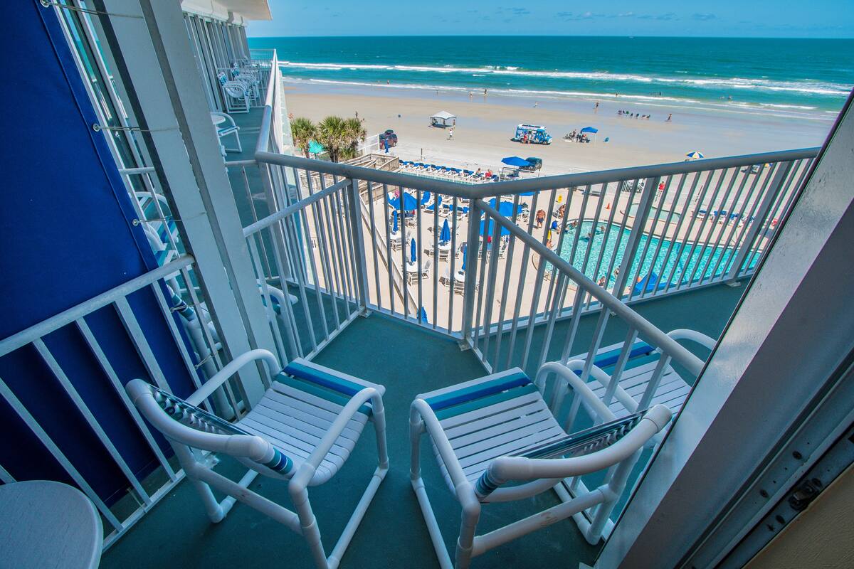 A balcony with white chairs and a pool area with blue umbrellas.