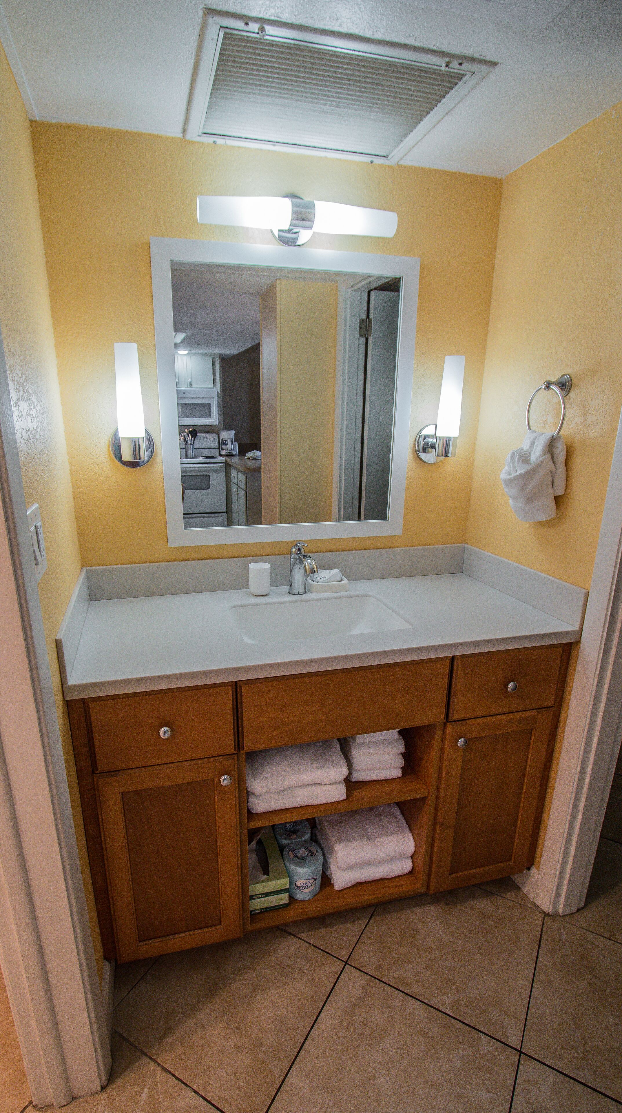 A bathroom with a white sink, wooden cabinets, a mirror, and a towel rack.