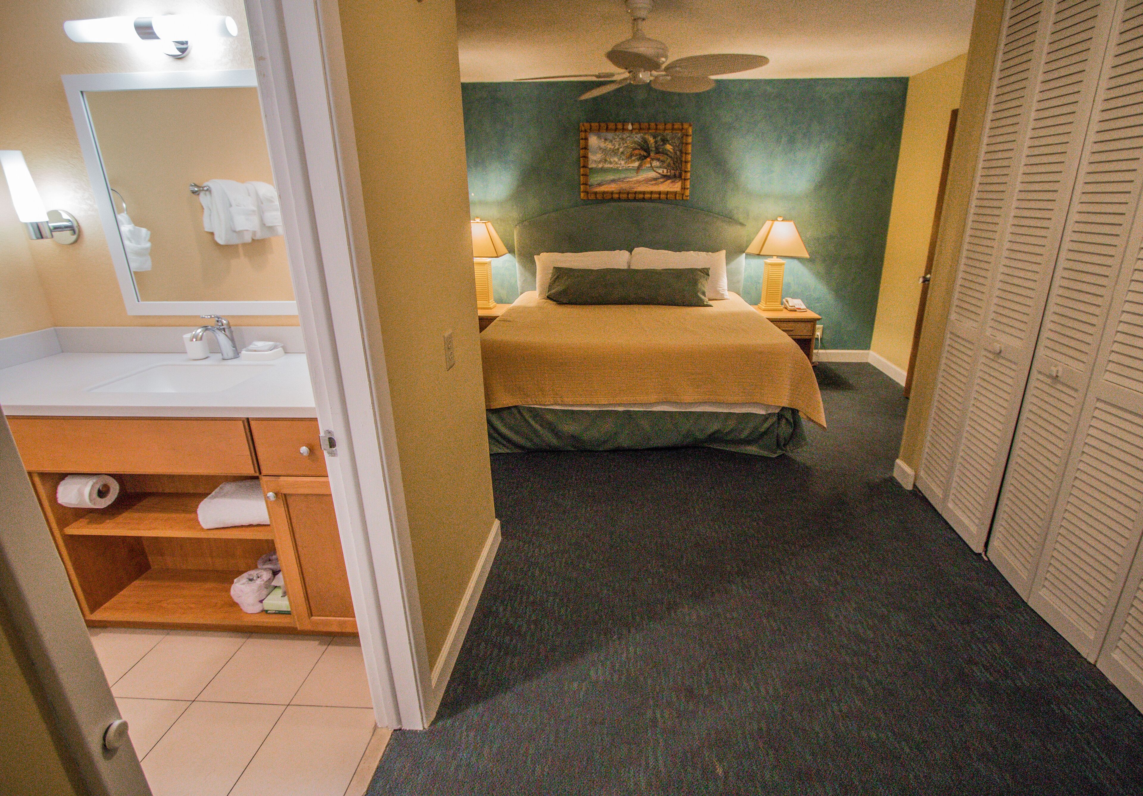 A hotel room with a bed, a bathroom with a sink, and a closet.