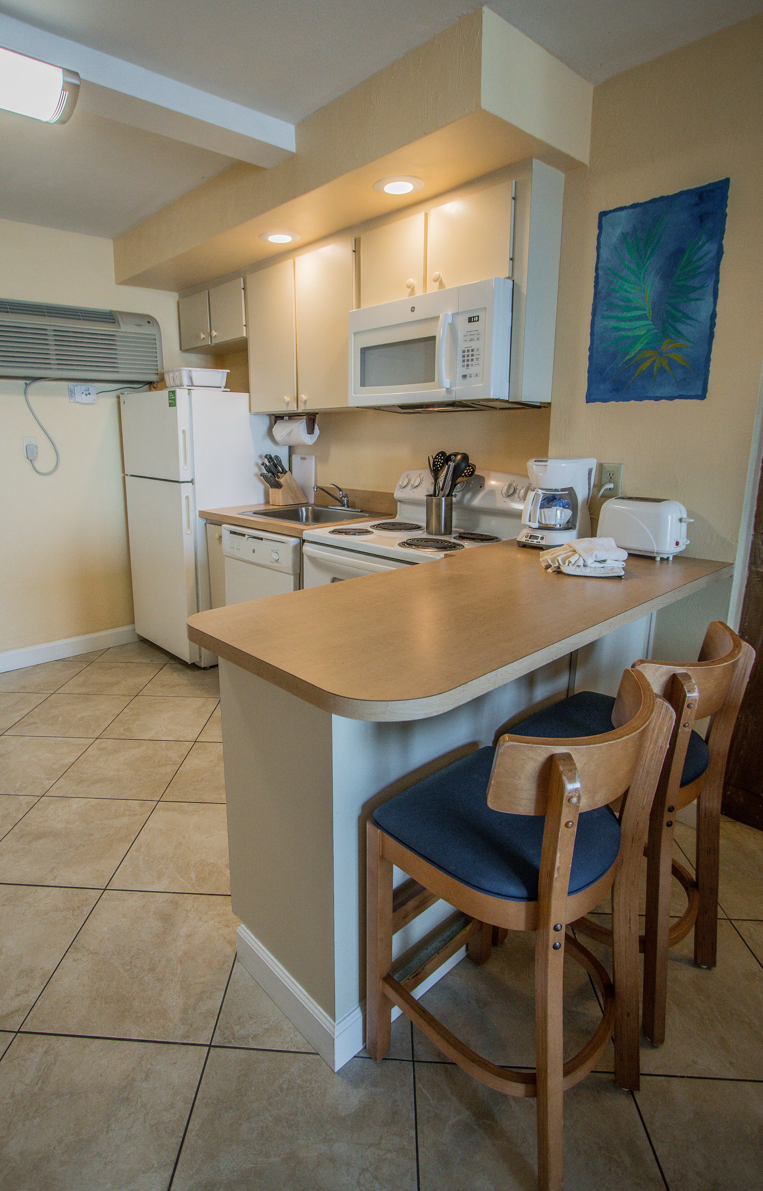 A kitchen with a central island, wooden chairs, a microwave, a refrigerator, and a coffee maker.