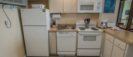 A compact kitchen with a refrigerator, microwave, stove, and dishwasher.