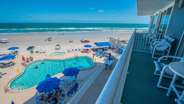 A pool area with lounge chairs and umbrellas, overlooking a beach and ocean. - Sea Club IV (Daytona Beach Shores)