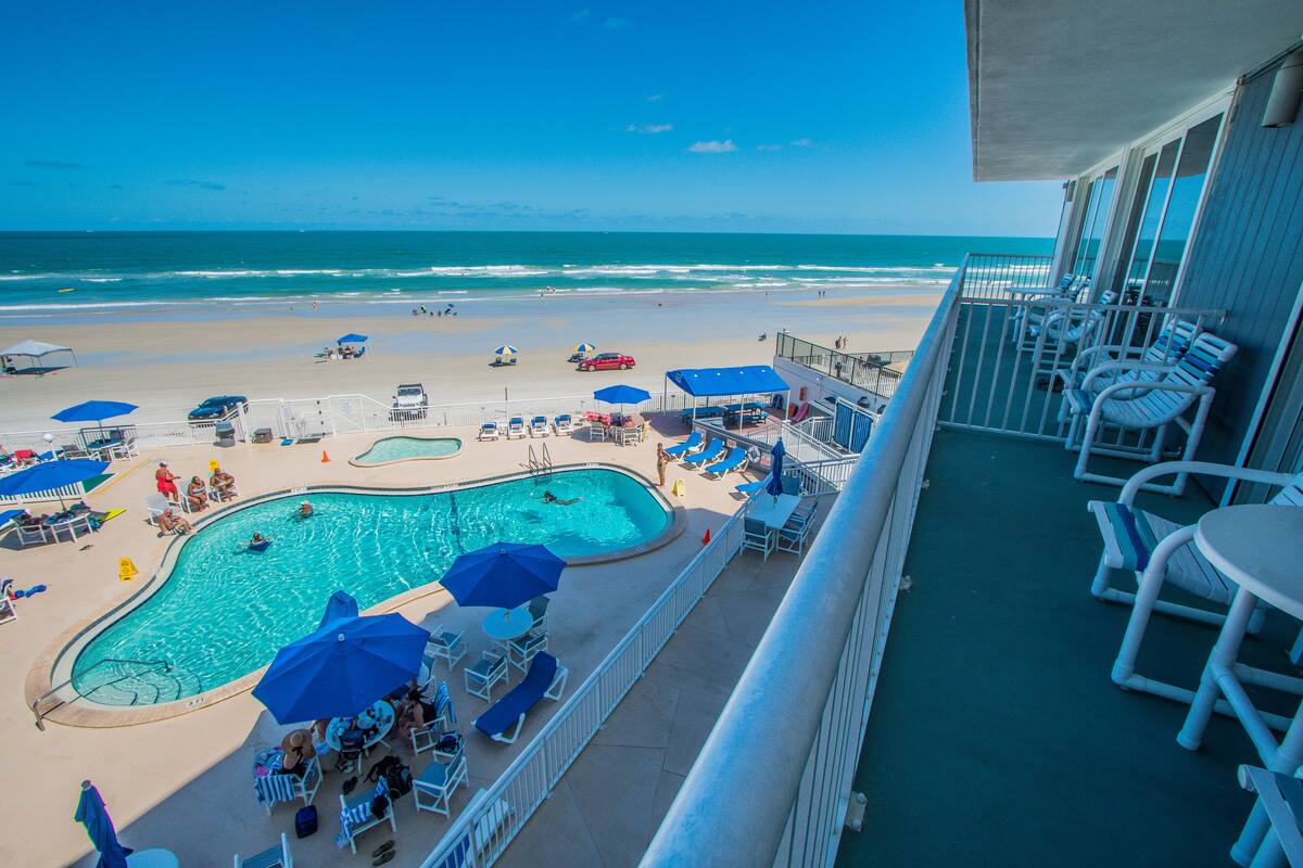 A pool area with lounge chairs and umbrellas, overlooking a beach and ocean.