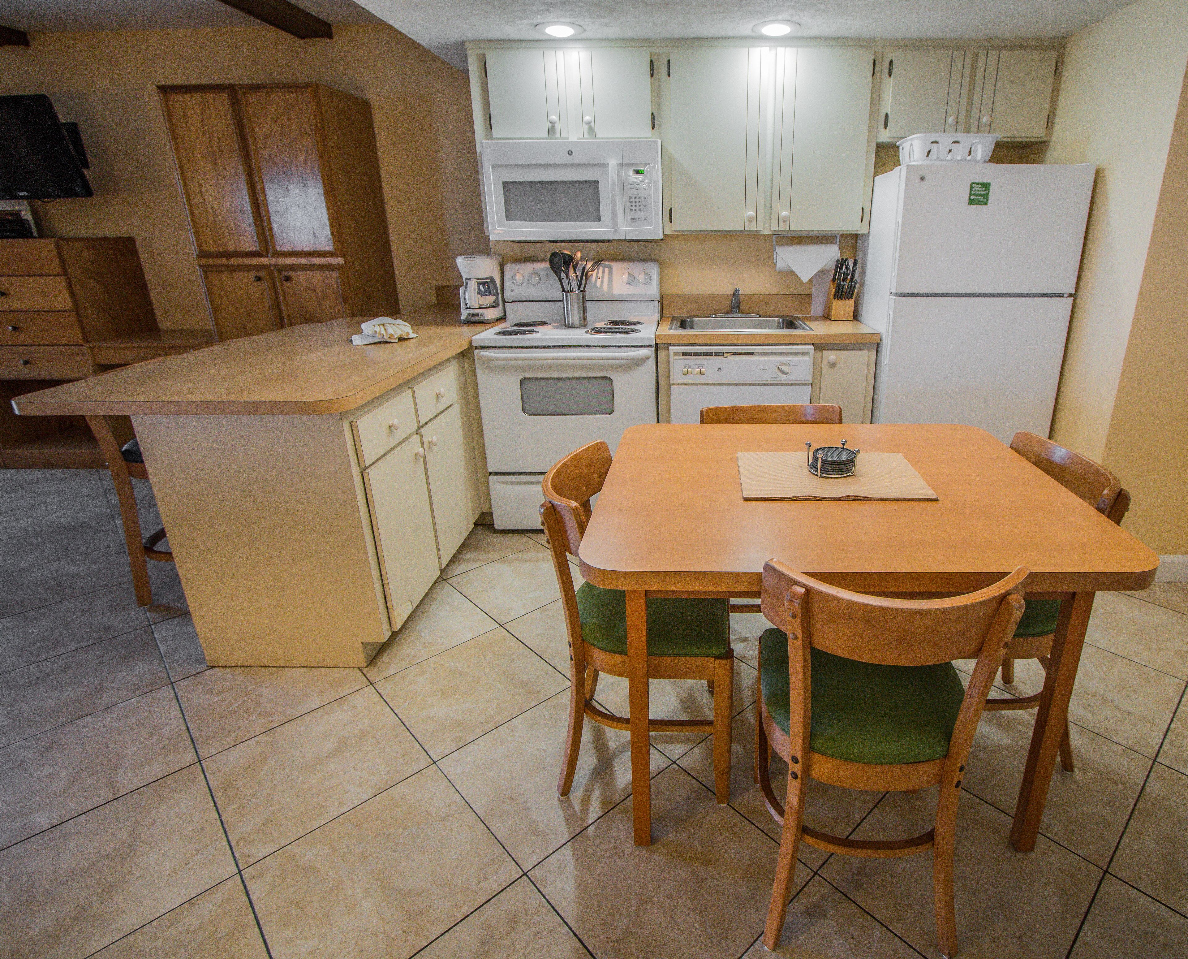 A compact kitchen with a central island, wooden chairs, and basic appliances.