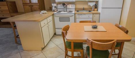 A compact kitchen with a central island, wooden chairs, and basic appliances.
