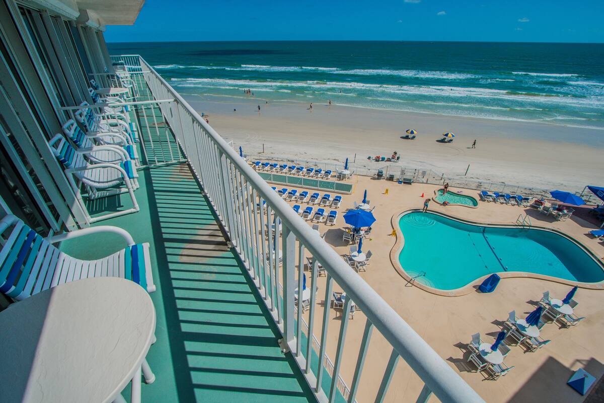 A balcony with rows of white lounge chairs and a pool area with blue chairs and umbrellas.