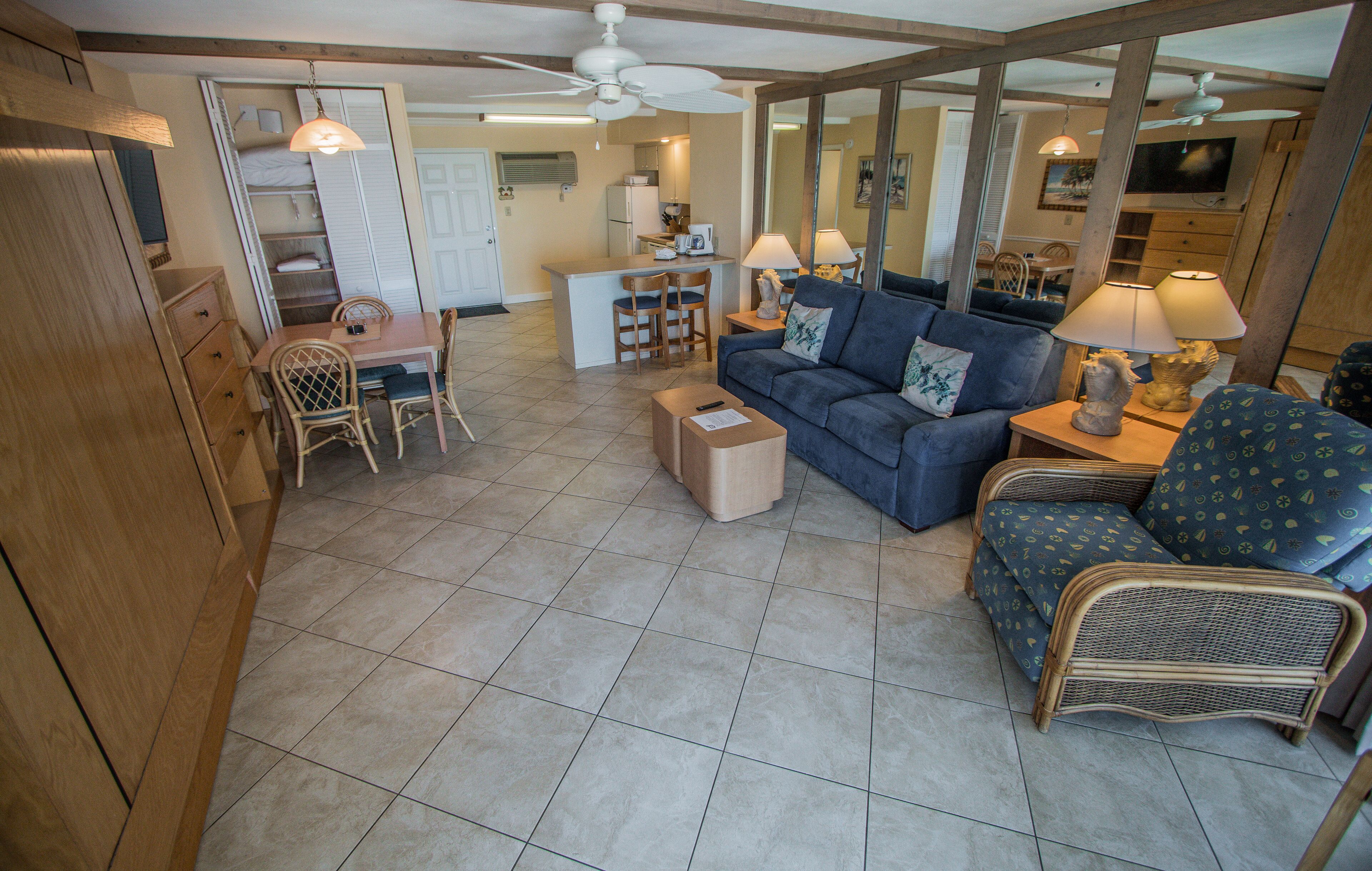 A spacious living area with a dining table, chairs, a sofa, and a small kitchen in the background.