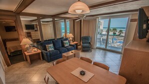 A hotel room with a balcony, a dining area, a sofa, and a TV. - Sea Club IV (Daytona Beach Shores)