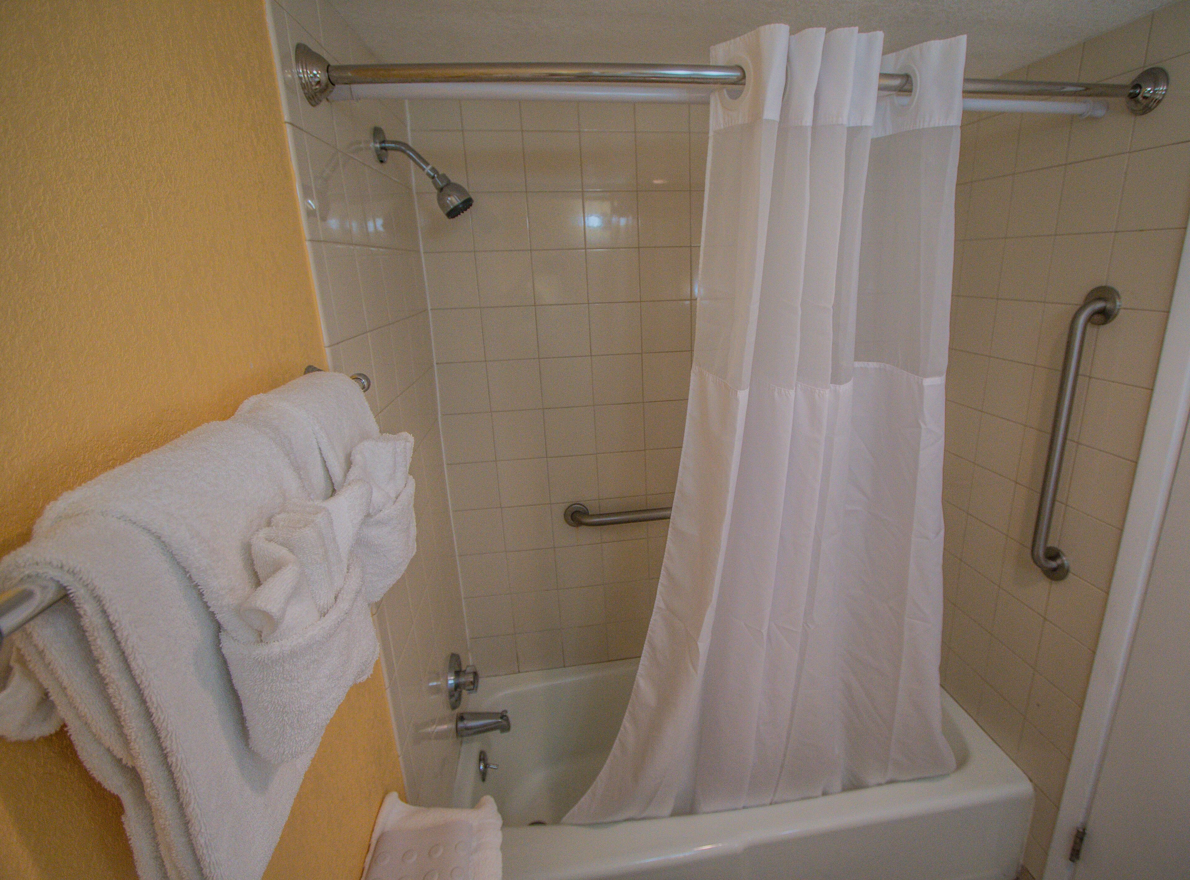A bathroom with a shower, grab bars, and a towel rack.