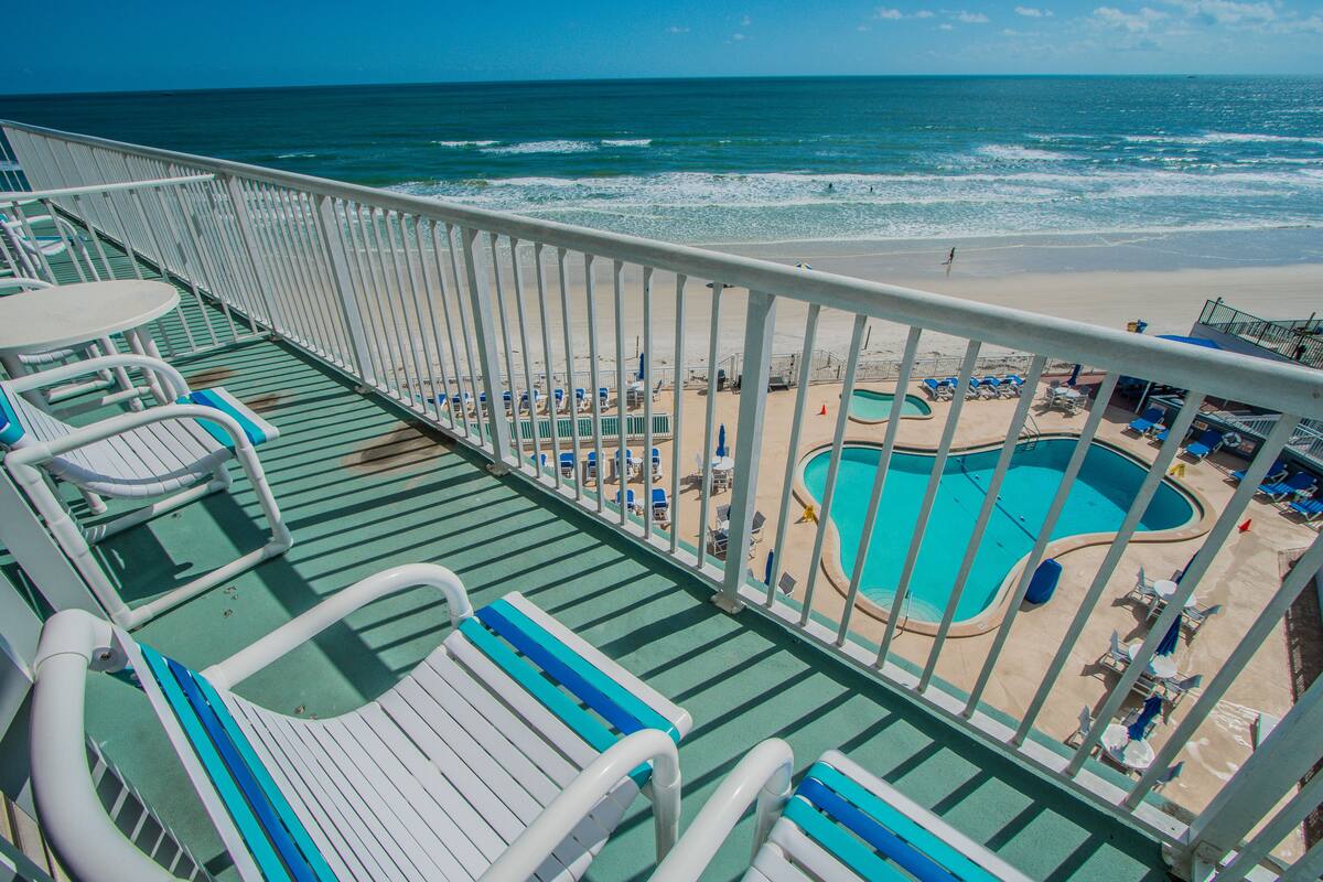 A deck with lounge chairs and a pool area with a view of the beach and ocean.