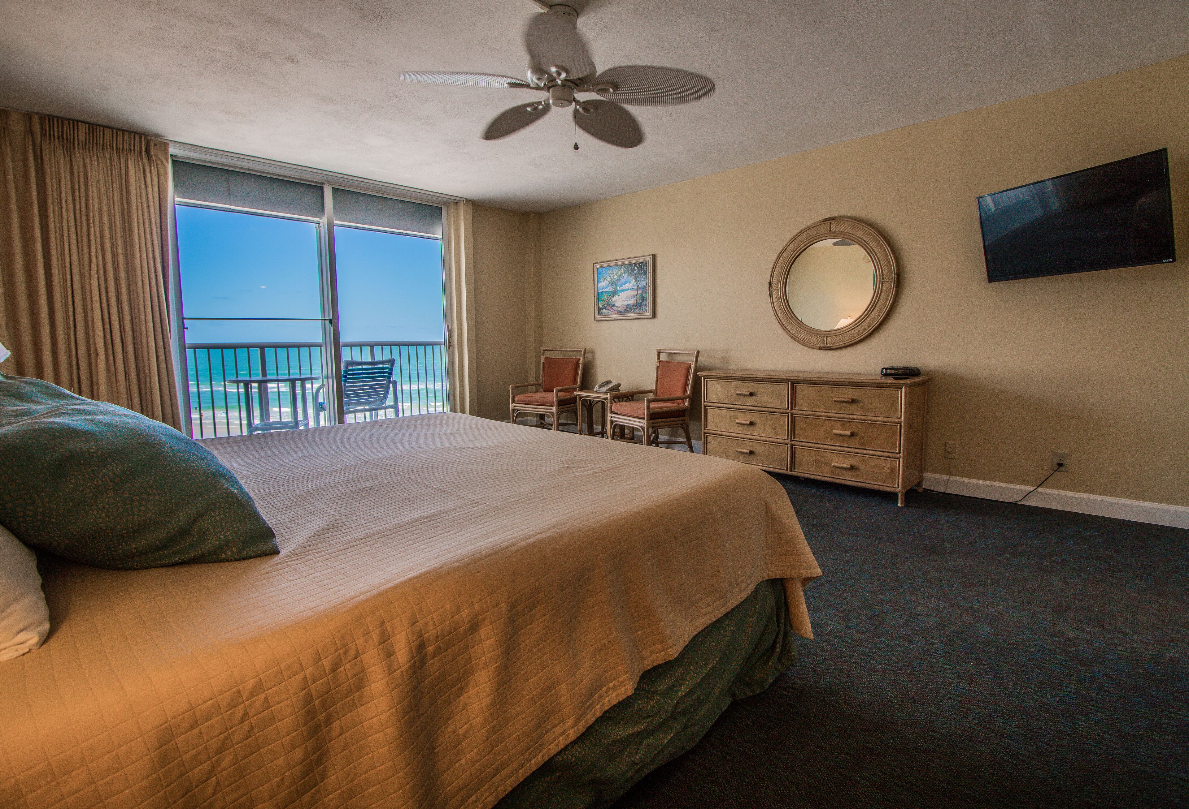 A hotel room with a bed, a desk, a chair, a television, a mirror, and a balcony with a view.