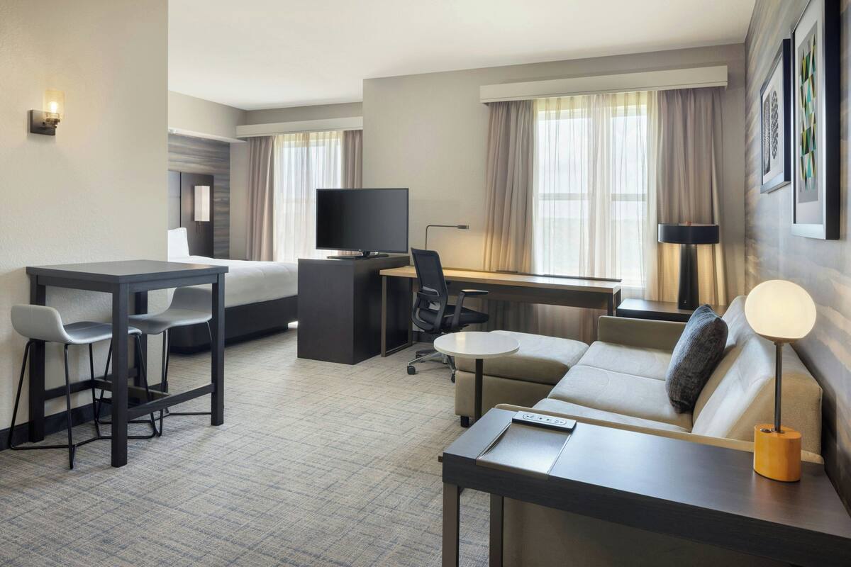 Una habitación de hotel con cama, escritorio con computadora, televisión, sofá y mesa de centro.