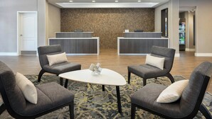 A reception area with two reception desks, a white round table, and four grey armchairs with white cushions. - Residence Inn Tampa Suncoast Parkway at NorthPointe Village (Lutz)