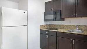 A kitchen with a white refrigerator, a microwave, dark cabinets, and a granite countertop. - Motel 6 Lancaster, TX - DeSoto - Lancaster (Lancaster)