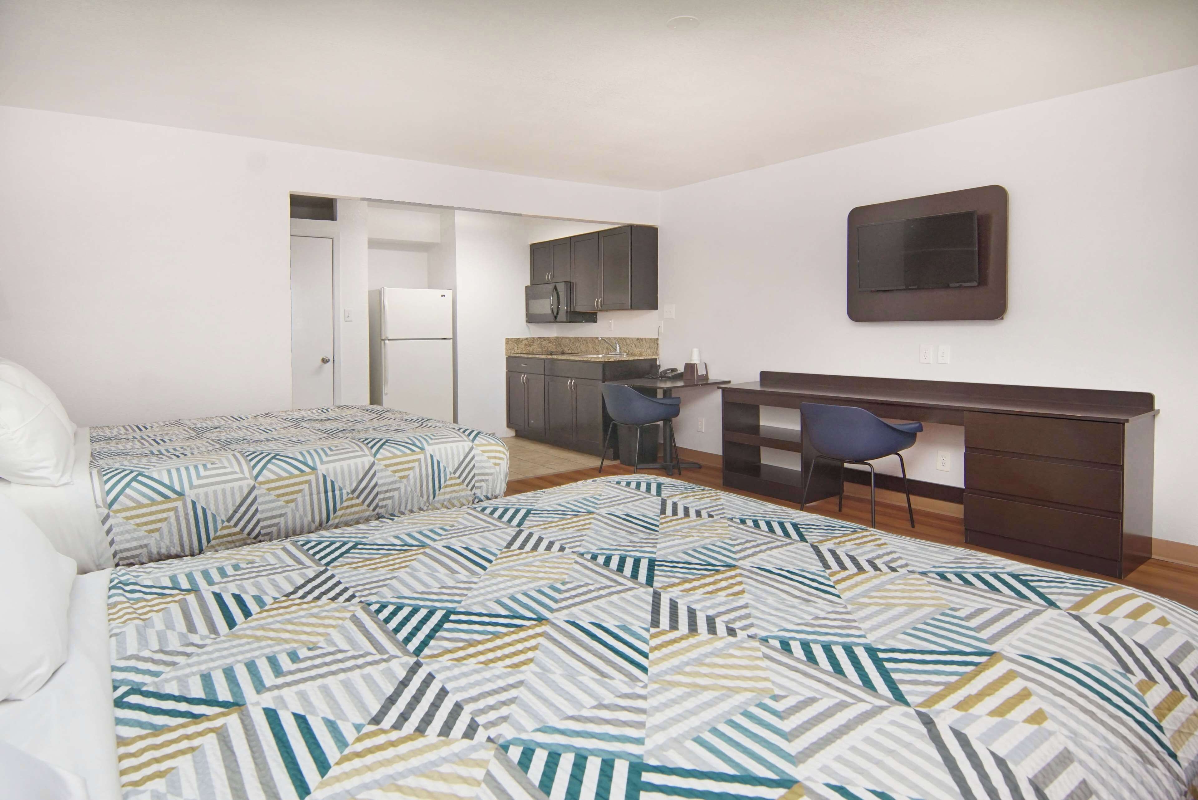 Un dormitorio con dos camas, un escritorio y una kitchenette.