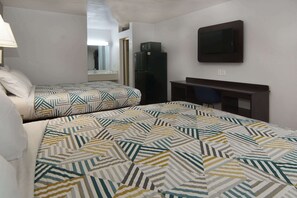 A hotel room with two beds, a desk, a television, and a refrigerator.