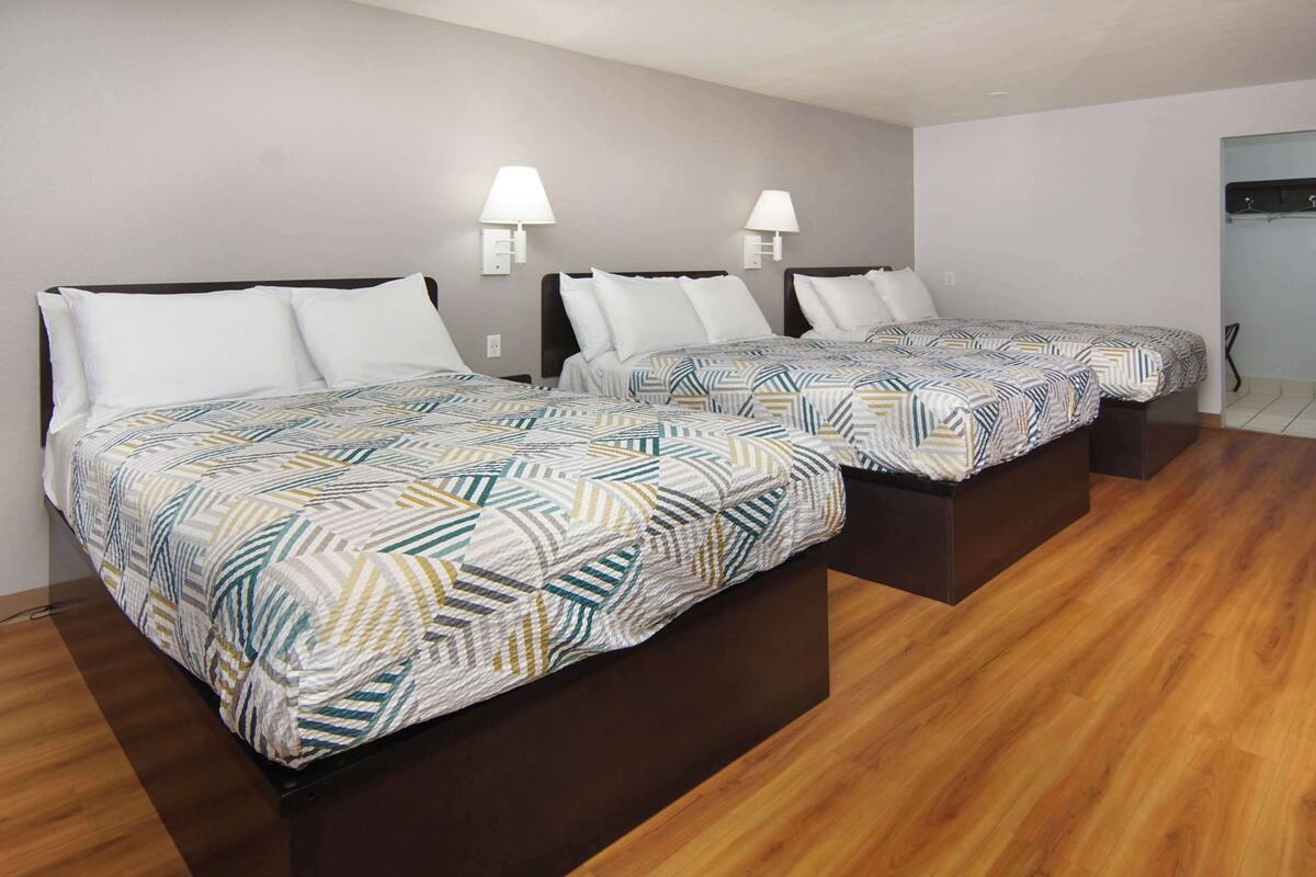 A hotel room with two beds, each with a patterned bedspread and white pillows. There are wall-mounted lamps on either side of the beds.