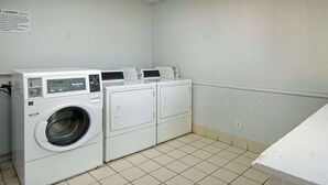 A laundry room with a front-loading washer and dryer, a sign with laundry rules, and a tiled floor. - Motel 6 Lancaster, TX - DeSoto - Lancaster (Lancaster)