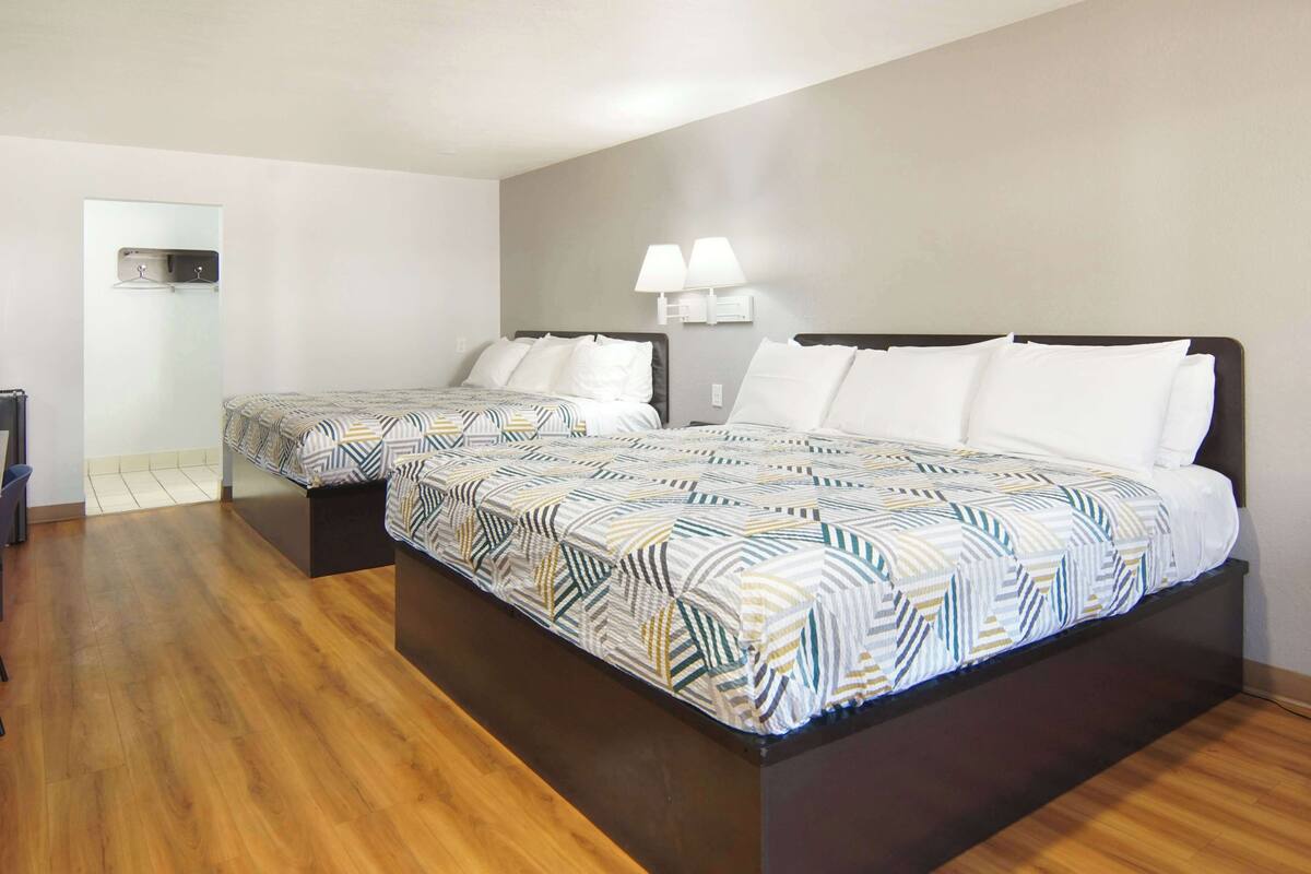 A hotel room with two beds, a wooden floor, a small desk, and a wall-mounted air conditioning unit.