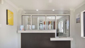 A reception area with a counter, a glass partition, and a clock on the wall. - Motel 6 Lancaster, TX - DeSoto - Lancaster (Lancaster)