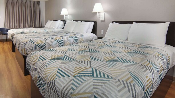 A hotel room with two beds, each with a patterned bedspread, a chair, and two wall-mounted lamps. - Motel 6 Lancaster, TX - DeSoto - Lancaster (Lancaster)