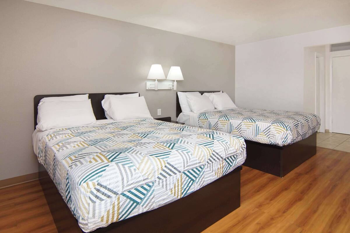 Two single beds with patterned bedding, a wall-mounted lamp, and a wooden floor.
