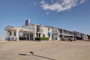 A motel with a '6' sign, multiple balconies, and a parking lot with several cars.