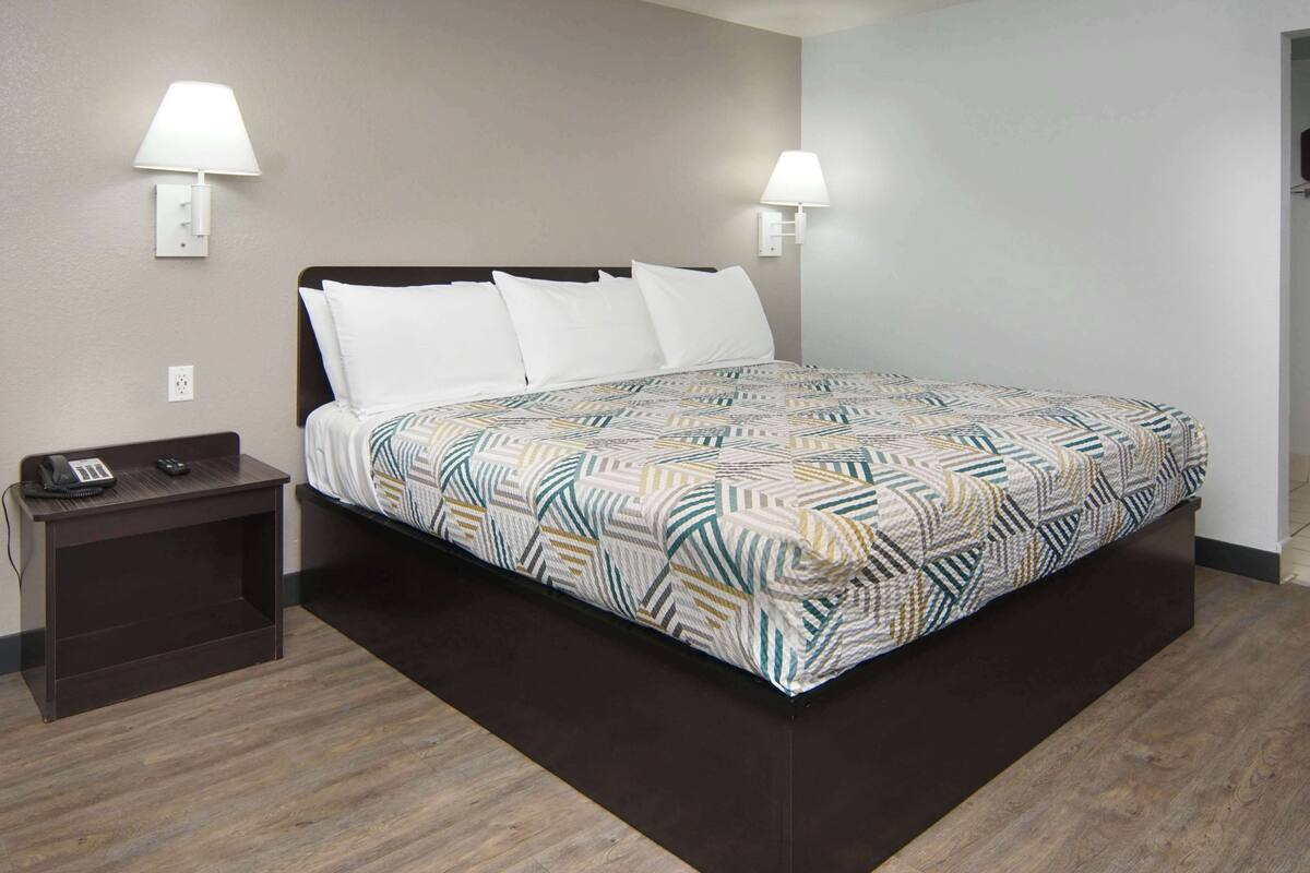 A hotel room with a bed, two bedside lamps, a nightstand with a phone, and a patterned bedspread.