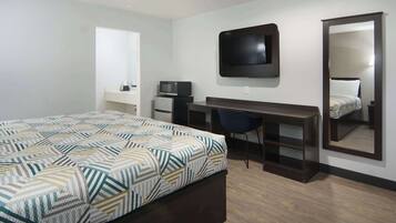 Quarto de hotel com uma cama, escrivaninha, cadeira, televisão, micro-ondas e um espelho grande.
