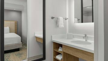 Un baño de hotel moderno con un espejo grande, lavabo blanco y tocador de madera.