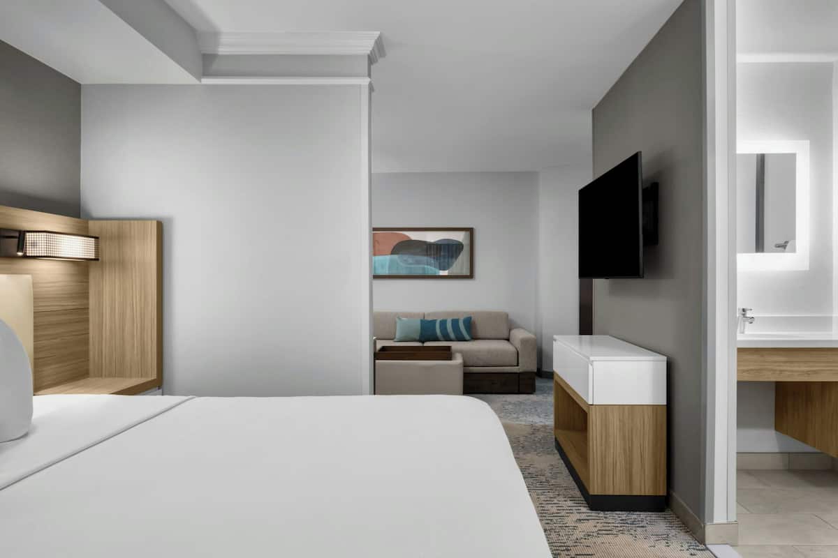 Ein modernes Hotelzimmer mit einem großen Bett, einem flachbildfernseher an der Wand, einer Couch und einem kleinen Beistelltisch.