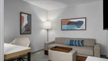 Una habitación de hotel moderna con sofá, una mesita, una lámpara y arte abstracto en las paredes.