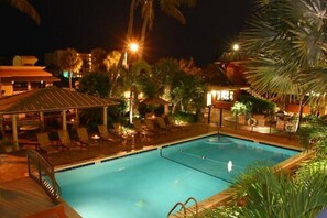 A nighttime swimming pool area with lounge chairs and umbrellas, surrounded by palm trees and buildings. - The Away Inn (Lauderdale-by-the-Sea)