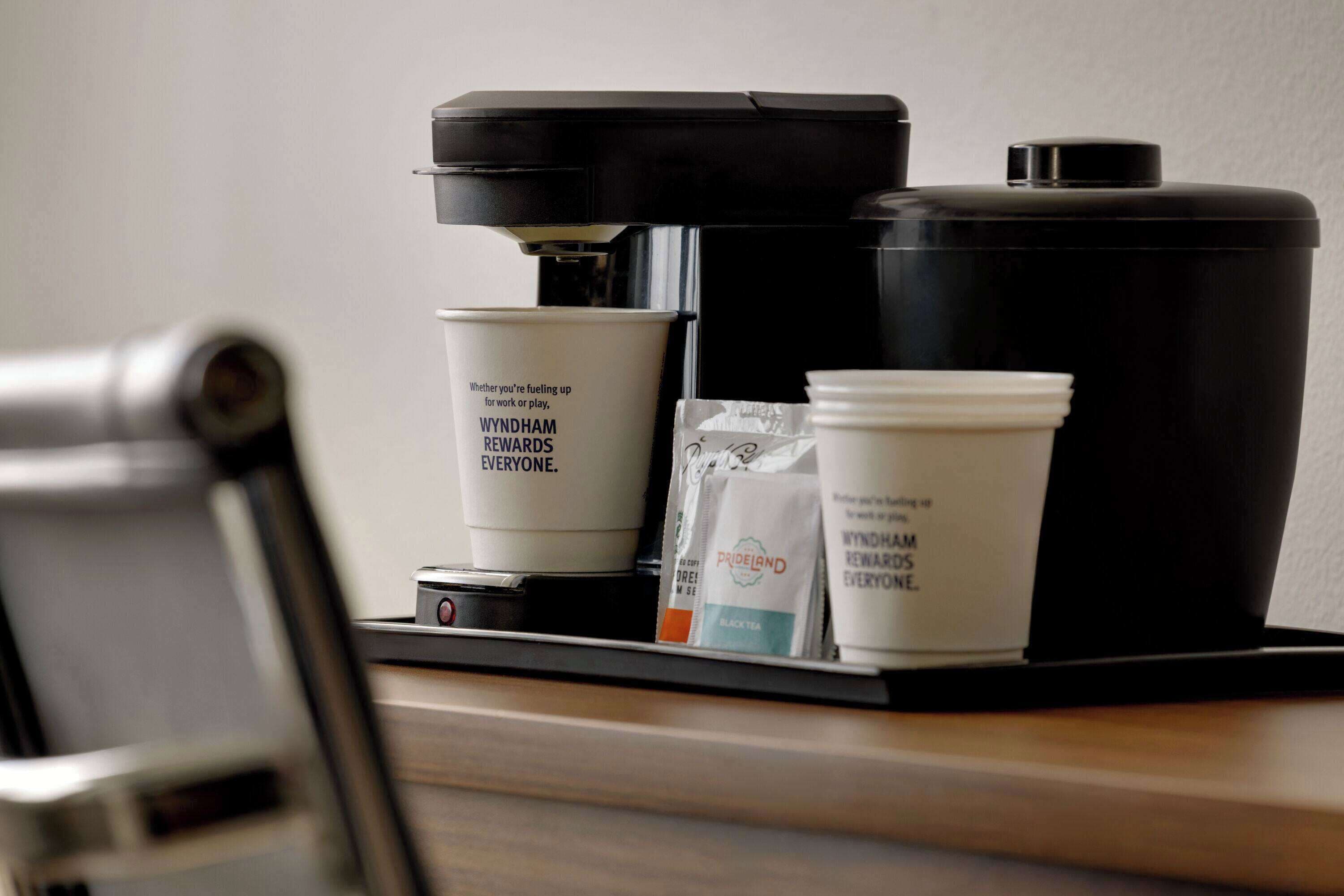 Eine Kaffeemaschine mit einem schwarzen Behälter und einer Kaffeetasse mit Schrift.