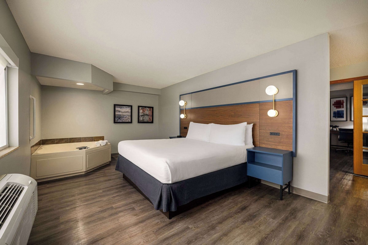 Una habitación de hotel moderna con una cama grande, un banco integrado, una bañera y una zona de escritorio.