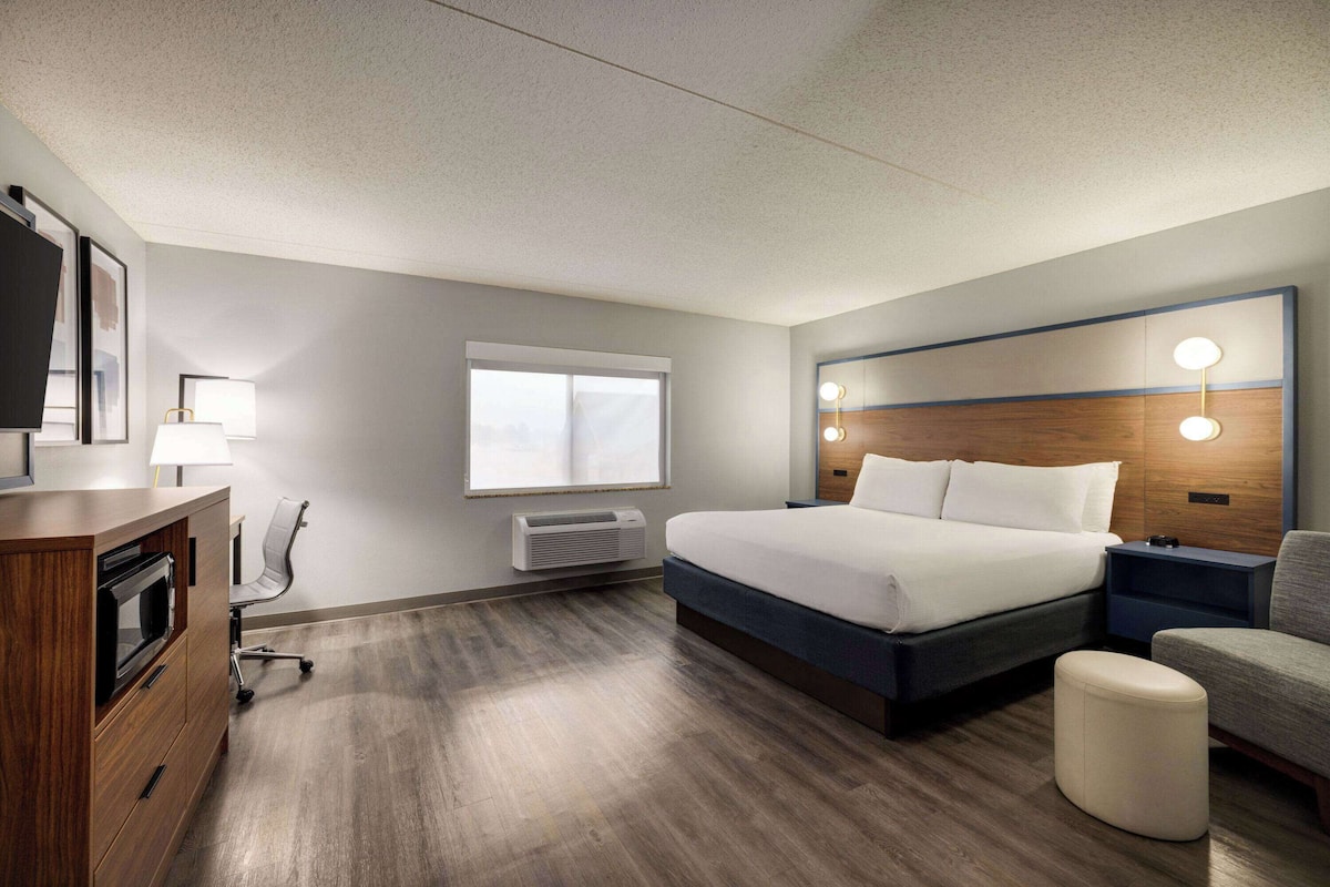 Una habitación de hotel con cama, mesita de noche, silla, escritorio y ventana.