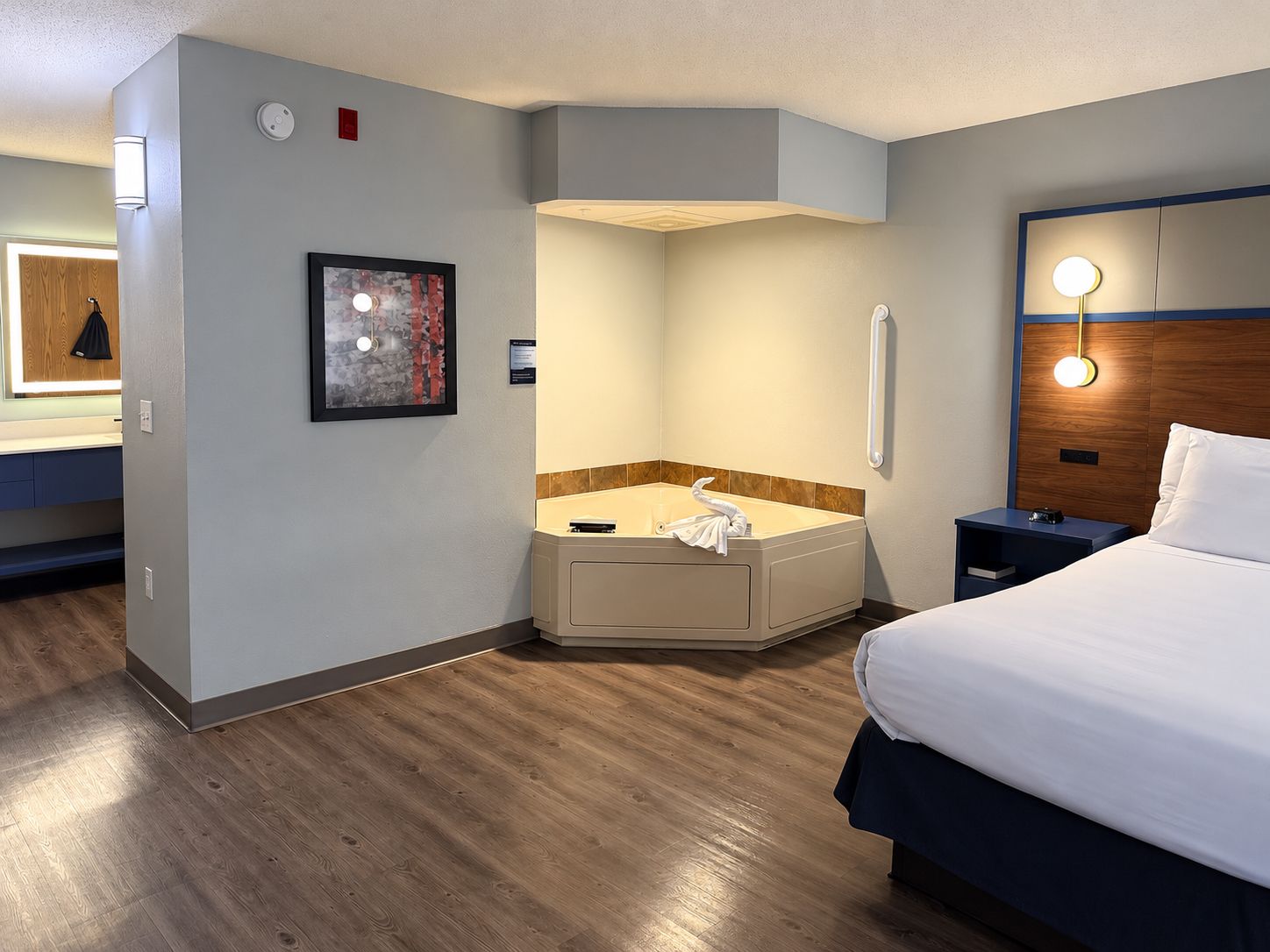 A hotel room with a bed, a bathroom with a bathtub, a bedside table, and a wall-mounted light fixture.