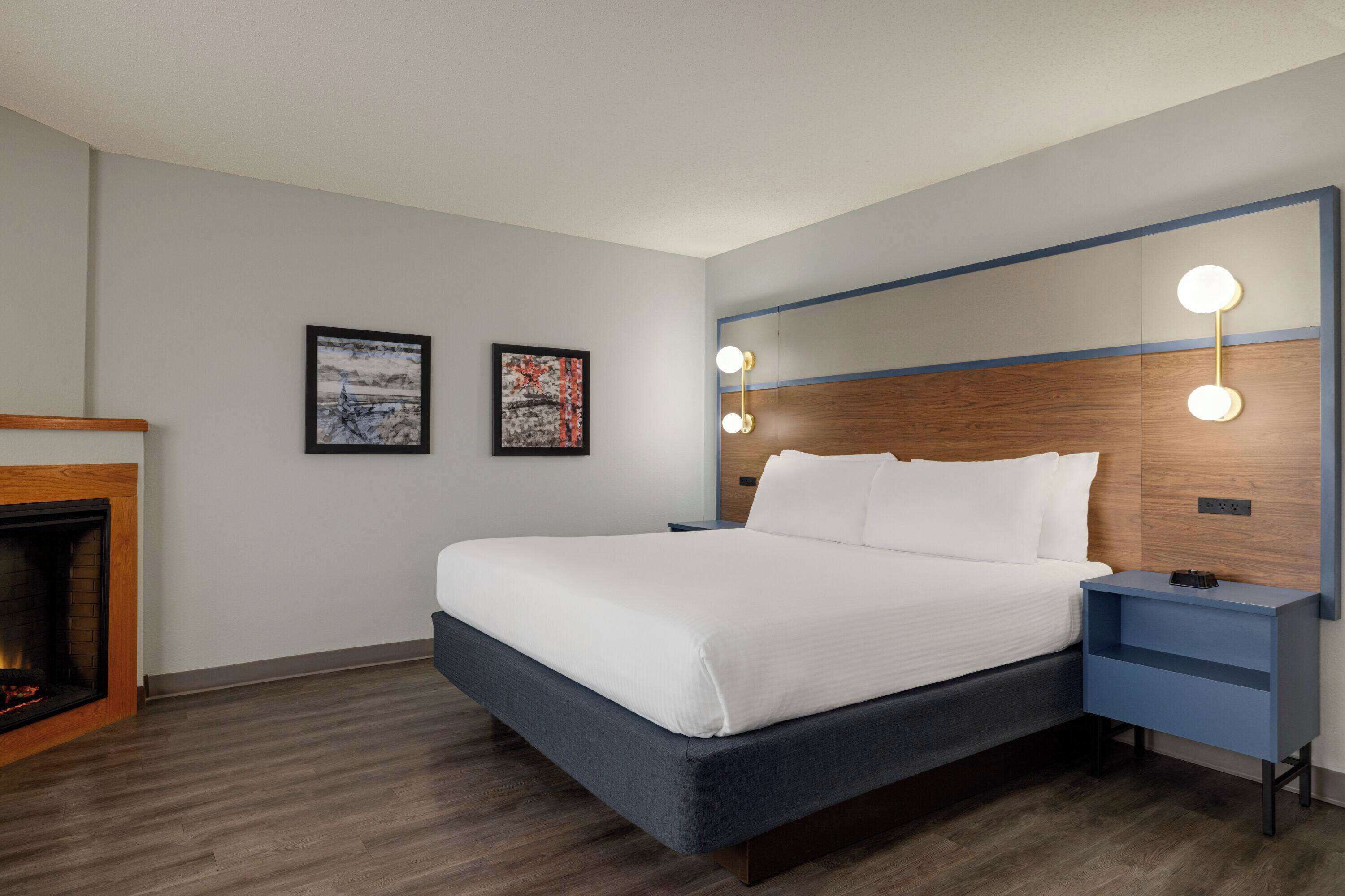 Une chambre d’hôtel moderne dotée d’un grand lit, de tables de chevet, d’une cheminée et de lampes fixées au mur.