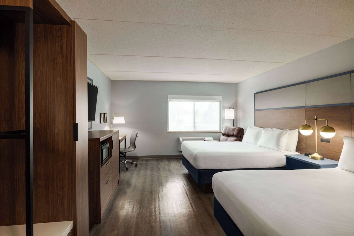 Habitación de hotel con dos camas, un escritorio con una silla, un televisor y una ventana.