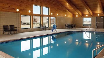 Una piscina interior con vigas de madera en el techo, paredes de azulejos y grandes ventanales.