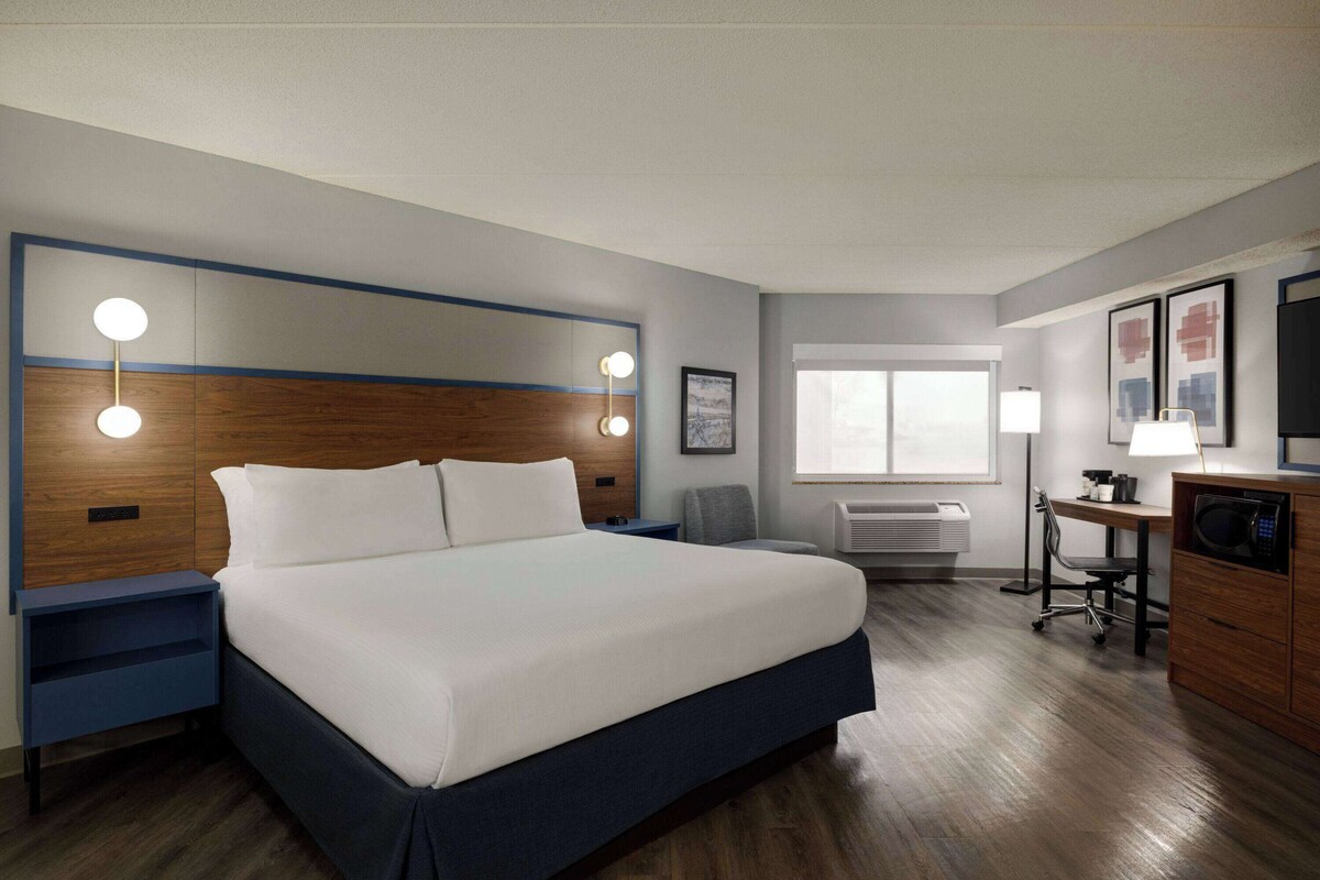 Ein Hotelzimmer mit einem großen Bett, Nachttischen, einem Schreibtisch mit Stuhl, einer Mikrowelle und einem Fenster.