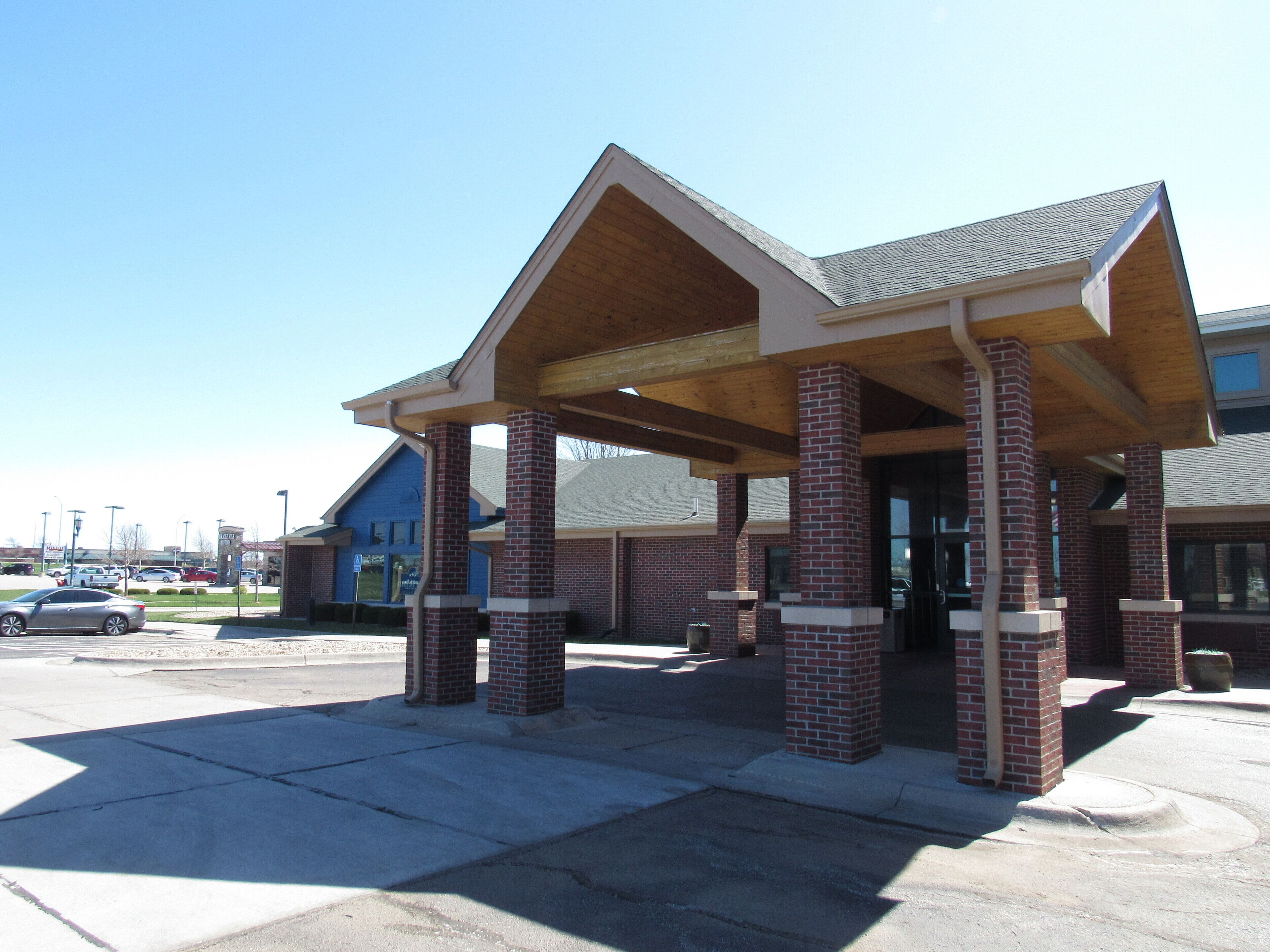 A building with a covered entrance area supported by brick pillars, a flat roof, and a clear sky in the background.