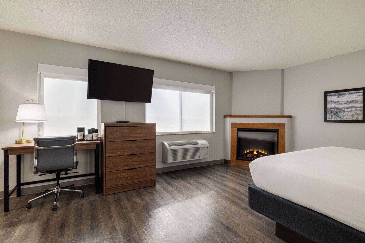 Ein Hotelzimmer mit Bett, Schreibtisch, Stuhl, Kommode, Fernseher, Kamin und großen Fenstern.