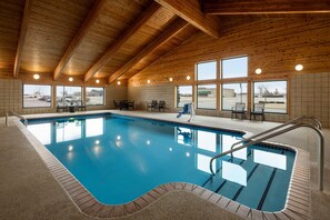 Una piscina interior con vigas de madera, paredes con azulejos y ventanas amplias.