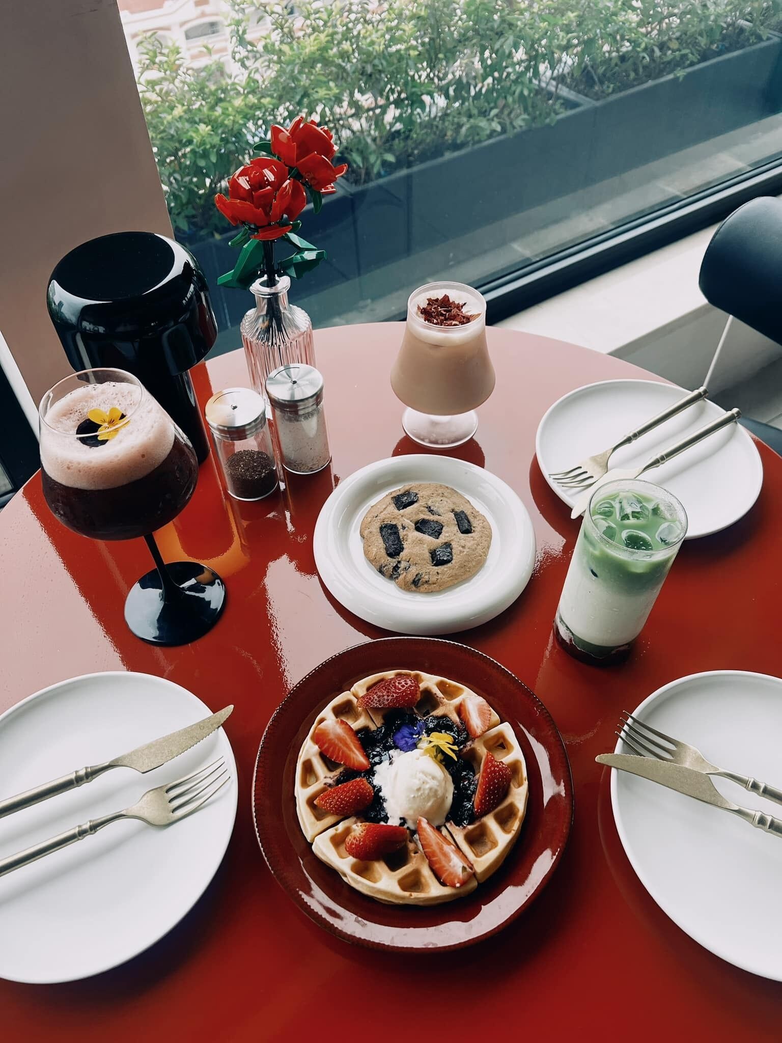 Uma mesa com diversos pratos e bebidas, incluindo waffles, um biscoito e um smoothie verde.