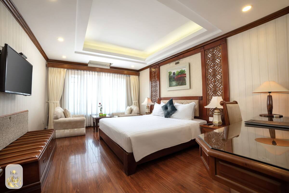Een hotelkamer met een groot bed, een flatscreen-televisie, een bank, een bureau en een lamp.