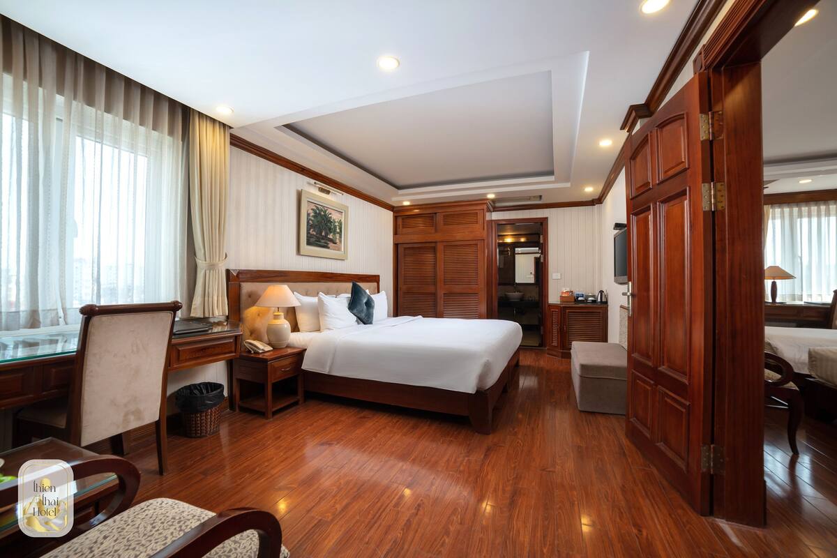 Hotelkamer met een groot bed, houten vloer, bureau met stoel, nachtkastje met lamp en een kledingkast.