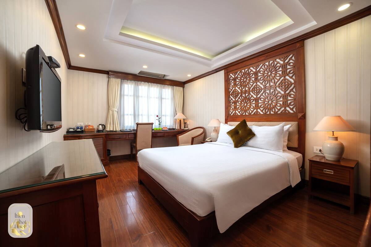 Hotelkamer met een groot bed, een bureau met stoel, een televisie en een decoratief wandpaneel.
