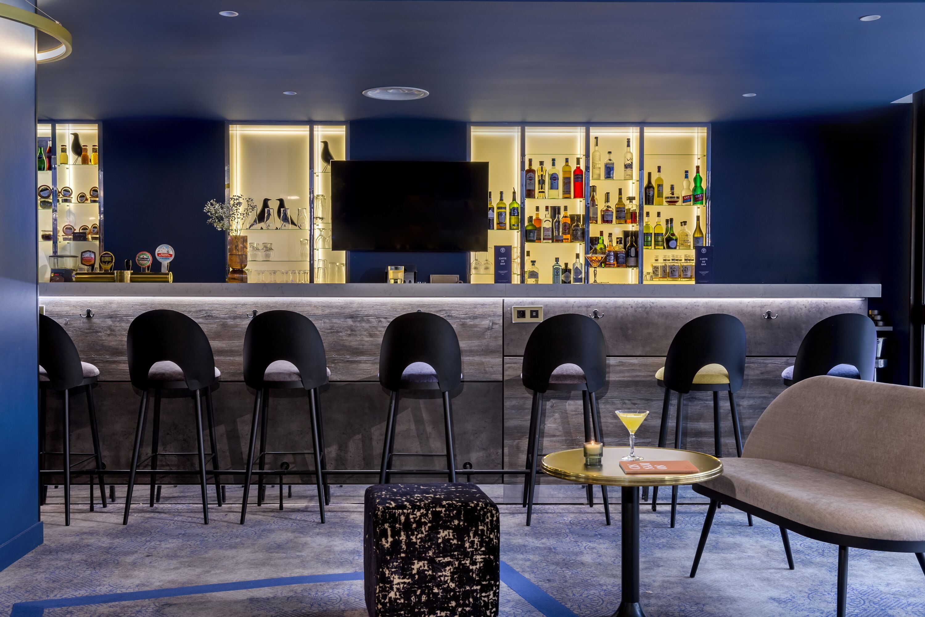 A bar area with a flat-screen TV, multiple bar stools, a round table with a martini glass, and a sofa.